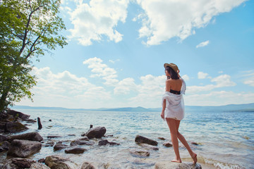 A slender woman in a white shirt and hat relaxes near the water