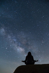 Fototapeta na wymiar Girl meditating in lotus pose under the beautiful Milky Way night sky