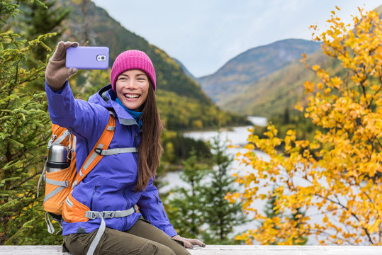 Mobile phone girl taking selfie photo on nature hike trail lifestyle. Happy Asian hiker woman holding smartphone selfie.