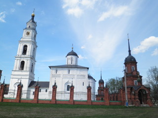 Fototapeta na wymiar white church with a bell tower behind a red brick fence with watchtowers against a blue sky with clouds