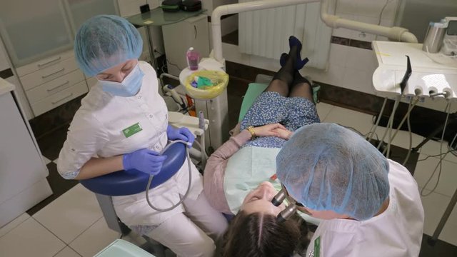 Woman at dentist clinic gets dental treatment to fill a cavity in a tooth. Dental restoration and composite material polymerization with UV light and laser. The doctor works with an assistant.