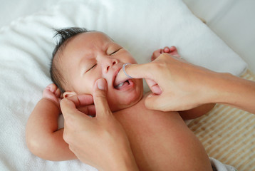 Close-up mother hand clean baby tongue and gum with soft rubber brush.