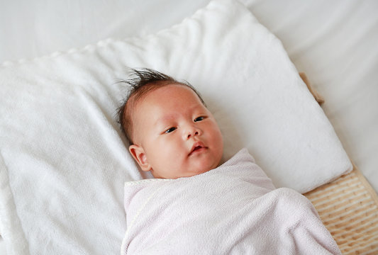 Infant baby boy in towel roll lying on bed after bath.