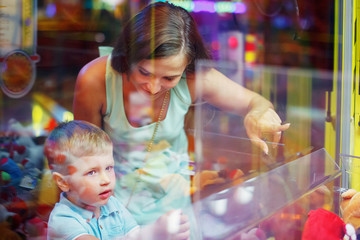 Cute boy in blue t-shirt with him young mother plays arcade in game machine at an amusement park.
