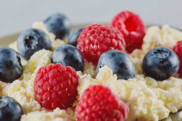 Cottage cheese with fresh raspberries and blueberries for a healthy breakfast with ripe berries. Background is a natural healthy product.