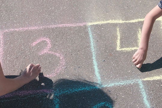 Mother and son draw numbers two and three on the hopscotch on asphalt.
