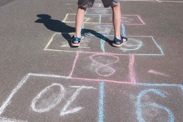 Boy jumps playing hopscotch in the street. Close-up legs.