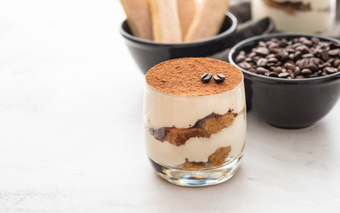 Traditional Italian dessert tiramisu in a glass on a white stone background. Copy space.