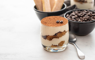 Traditional Italian dessert tiramisu in a glass on a white stone background. Copy space.
