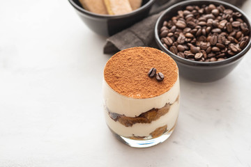Traditional Italian dessert tiramisu in a glass on a white stone background. Copy space.