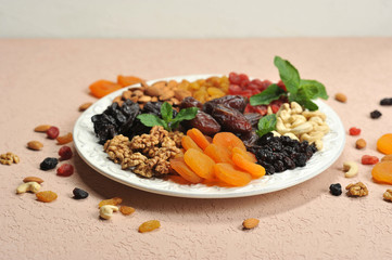 Nuts and dried fruits on a large white dish. On a plate of raisins, dried apricots, prunes, dates, cherries, cashews, almonds, walnuts. Light background. Close-up. 
