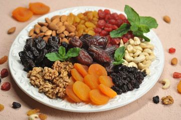 Nuts and dried fruits on a large white dish. On a plate of raisins, dried apricots, prunes, dates, cherries, cashews, almonds, walnuts. Light background. Close-up. 