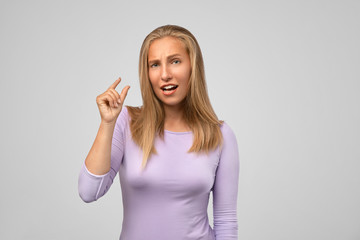 Woman showing small amount of something with fingers, isolated on gray background. Too small. Beautiful young woman gesturing small size with her fingers