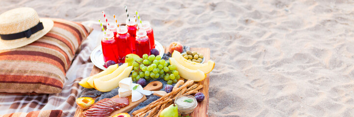 Picnic on the beach at sunset in the style of boho. Concept outdoors evening healthy dinnner with fruit and juice