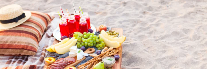 Photo sur Plexiglas Pique-nique Picnic on the beach at sunset in the style of boho. Concept outdoors evening healthy dinnner with fruit and juice