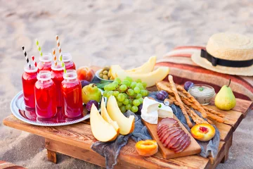 Papier Peint photo autocollant Pique-nique Picnic on the beach at sunset in the style of boho. Concept outdoors evening healthy dinnner with fruit and juice