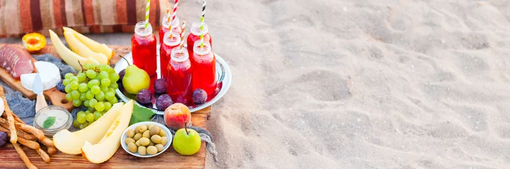 Photo sur Plexiglas Pique-nique Pique-nique sur la plage au coucher du soleil dans le style bohème. Concept de dîner sain en plein air avec des fruits et des jus de fruits