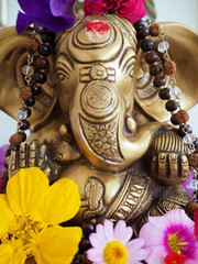 Hindu God Ganesha is covered with coloured flowers on an altar for a spiritual ceremony 