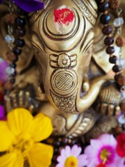 Fototapeta na wymiar Hindu God Ganesha is covered with coloured flowers on an altar for a spiritual ceremony 