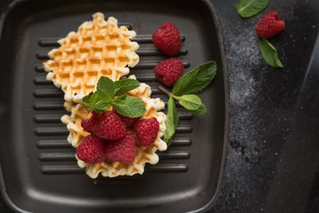 Belgian waffles with raspberries on the black table with sugar powder. Decorated with mint leaves. Healthy breakfast. 