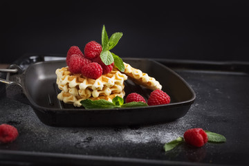 Belgian waffles with raspberries on the black table with sugar powder. Decorated with mint leaves. Healthy breakfast. 