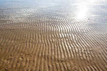 Wavy sand texture on sandy beach at low tide in the evening on hot summer day