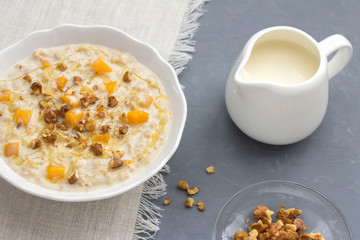 Pumpkin oatmeal with honey and nuts, milk in a milkman, walnuts on a gray background. healthy delicious homemade breakfast