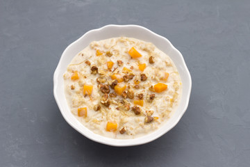Pumpkin oatmeal with honey and nuts, milk in a milkman, walnuts on a gray background. healthy delicious homemade breakfast