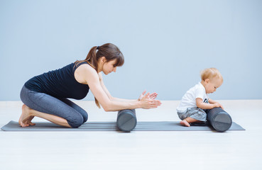 Young mother workout with foam rollers does physical pilates exercises together with her toddler baby boy. Fitness, happy maternity sport with children concept.