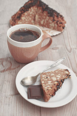 Piece of cake and chocolate on white plate with spoon and cup of coffee on natural wooden table vintage tone at shallow depth of field.