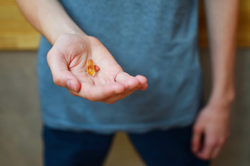 Man hand holding fish oil Omega-3 capsule and vitamins pill daily dose on blurred background. Medical healthcare, healthy nutrition supplements concept.