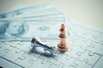 Golden king chess piece win the silver king chess on the game with puzzle and banknotes background for business and financial concept.