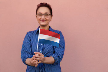 Netherlands flag. Woman holding the Netherlands Holland flag. Nice portrait of middle aged lady 40 50 years old with a national Dutch flag over pink wall background.