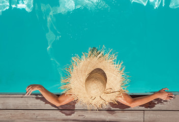 Woman in big straw hat sitting in the swimming pool