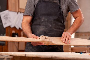 Experienced carpenter in work clothes and small buiness owner working in woodwork,  holding wood, on background  worktable in workshop