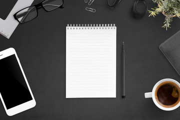 Notebook on black desk surrounded with office accessories. Blank paper, flat lay.