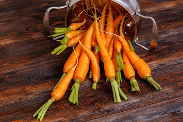 Fresh ripe carrot bunch on rustic wooden background, metal pot