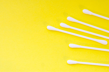 White cotton swabs or buds are on yellow uniform background view from above with clear area of half of photo for labels or headers. Hygienic products for cleaning ears, aural hygiene and cosmetics 