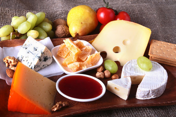Assortment of cheese with fruits, grapes and nuts on a wooden serving tray.