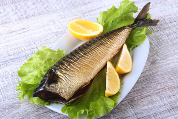 Smoked mackerele and lemon on green lettuce leaves on Wooden cutting board isolated on white background.