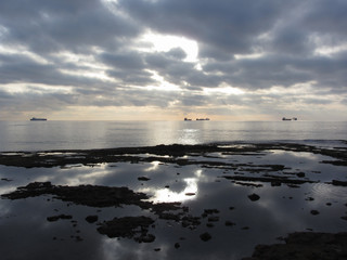 Fototapeta premium Rocks lunar landscape sea with giants cumulonimbus clouds in the sky and cargo ships at the horizon . Tuscany, Italy