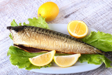 Smoked mackerele and lemon on green lettuce leaves on Wooden cutting board isolated on white background.