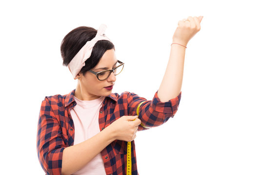Pretty pin-up girl wearing glasses measuring her biceps.