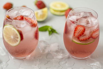 Glass of strawberry lemonade with pieces of strawberry, lime and fresh mint. Fresh summer bright cocktail.