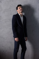 Obraz premium A happy handsome young businessman in a black suit standing in front of a grey wall in a studio.