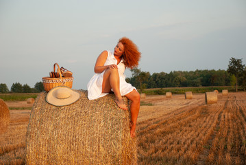 Red-haired woman posing on the field near a haystack