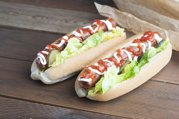 Two homemade Hot Dogs with mayonnaise, ketchup, and green lettuce leaves decorated with baking paper, over wooden table.