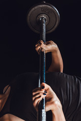 cropped image of female athlete doing exercise with barbell at gym, black background