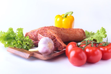 Raw pork knuckle and vegetables, garlic, tomatoes, bell pepper. spices and lettuce leaves on a cutting board. Selective focus. Ready for cooking.