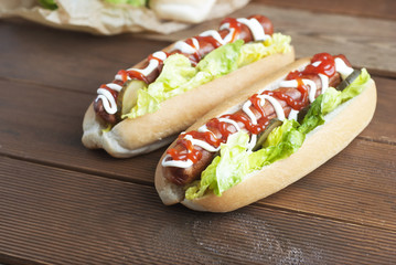 Two homemade Hot Dogs with mayonnaise, ketchup, and green lettuce leaves decorated with baking paper, over wooden table.